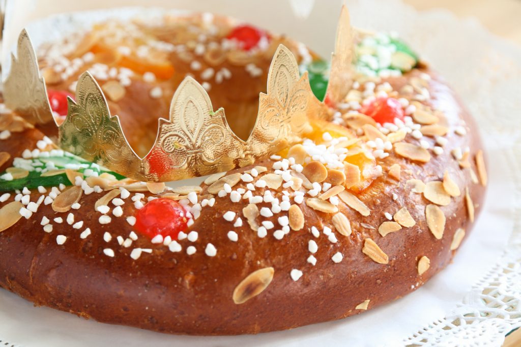 Ein Roscón de Reyes ist mit Hagelzucker, Mandelblättchen und kandierten Früchten dekoriert und trägt eine goldene Papierkrone.