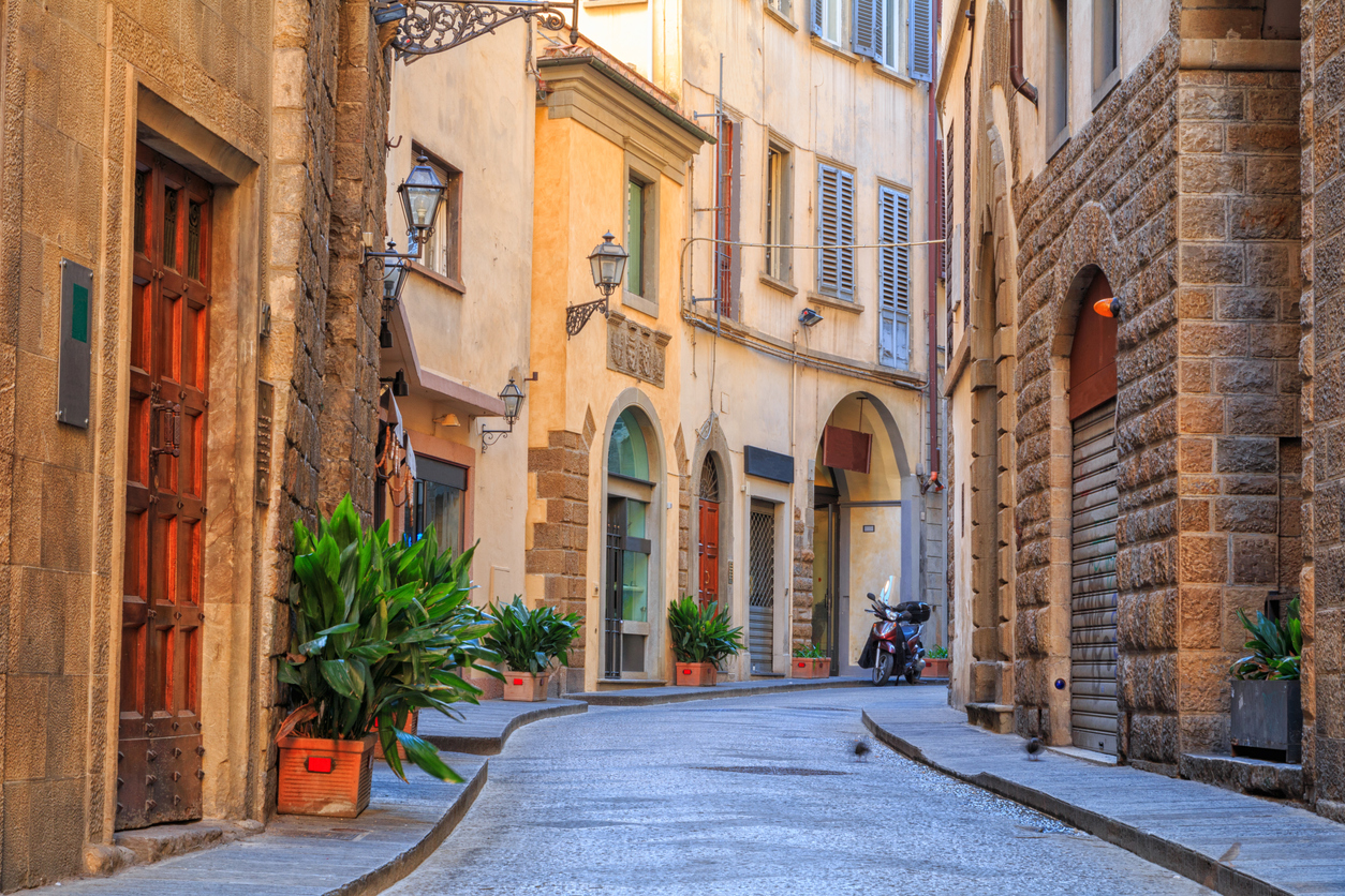 Eine schmale Gasse mit warmen Fassaden, Laternen und Pflanzen führt durch die Altstadt von Florenz.