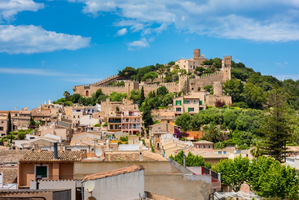 Panoramablick auf Capdepera mit Burganlage, Häusern und grünem Hügel.