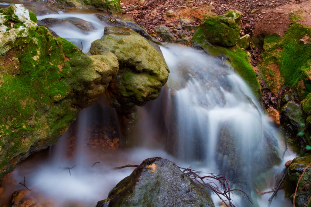 Bachlauf am Salt des Freu auf Mallorca mit kleiner Kaskade zwischen großen, grünen Felsen.