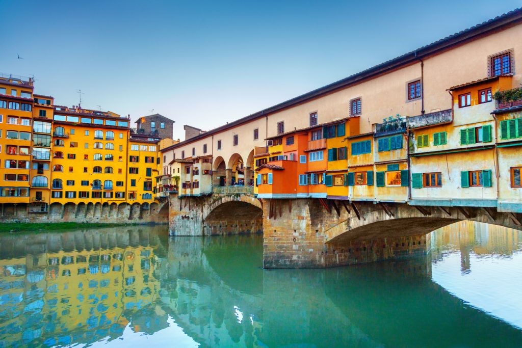 Die Ponte Vecchio mit bunten Häusern liegt über dem ruhigen Arno in Florenz.