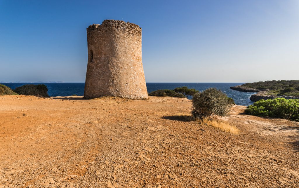 Die Torre de Cala Pi steht allein auf trockenem Boden mit Meerblick im Hintergrund.