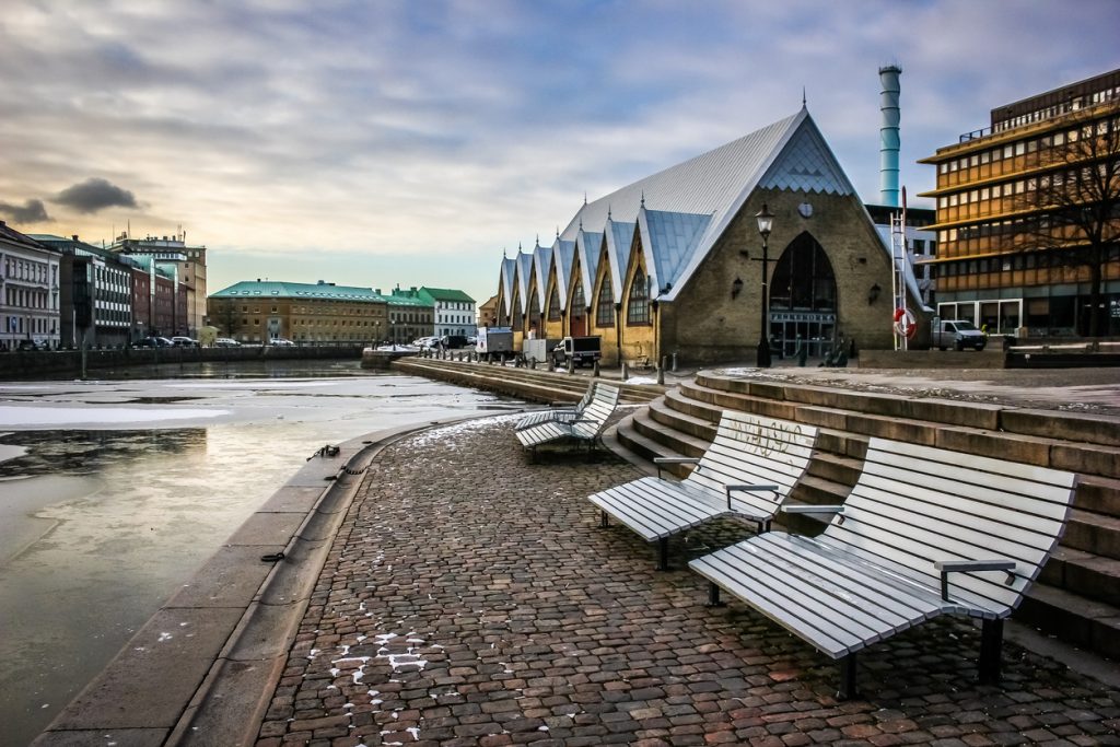 Bänke und Kopfsteinpflaster liegen am Kanal neben einem großen Gebäude mit steilem Dach.