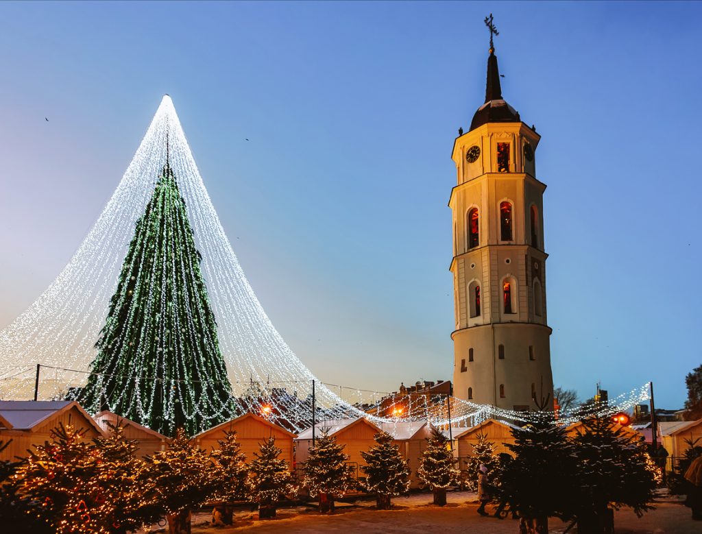 Ein großer beleuchteter Weihnachtsbaum und der Kirchturm stehen über einem Markt mit Lichterketten.