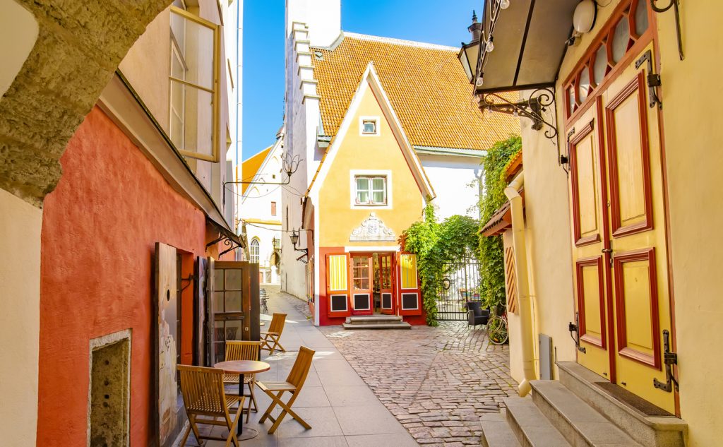 Enge Altstadtgasse mit farbigen Häusern, Kopfsteinpflaster und Sitzgelegenheiten.