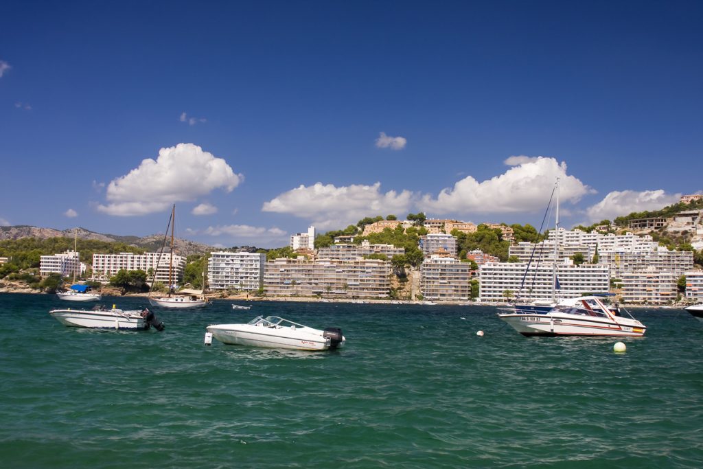 Mehrere Boote liegen auf dem Wasser, im Hintergrund stehen Gebäude entlang der Küste.