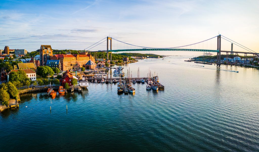 Ein kleiner Hafen mit Segelbooten liegt vor einer großen Brücke über breitem Wasser.
