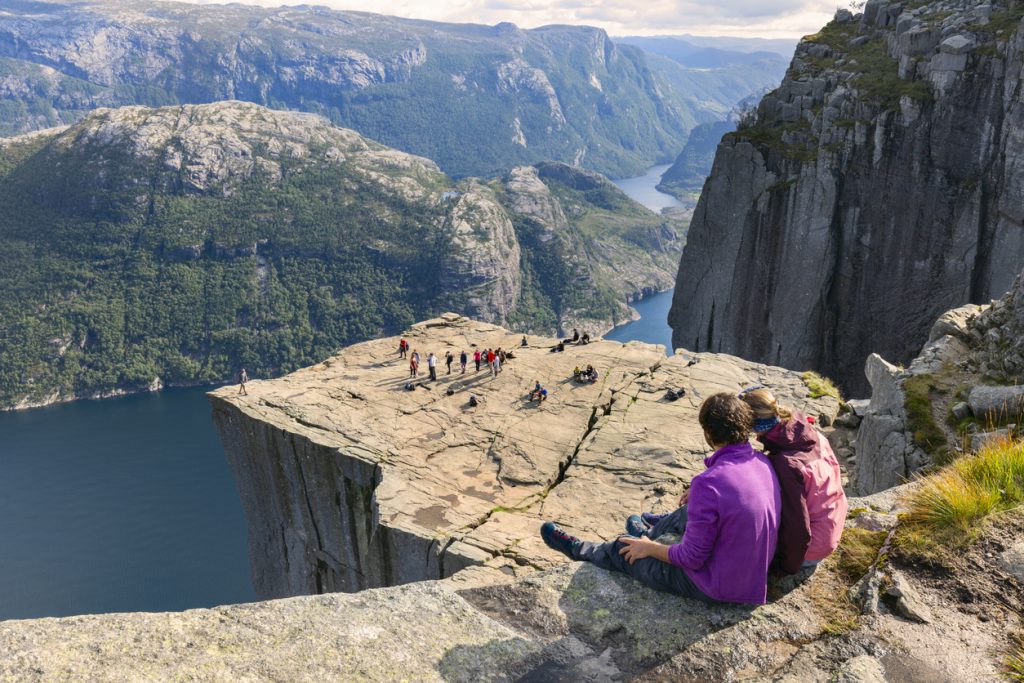 Große Felsplattform hoch über einem Fjord mit vielen Menschen und steilen Wänden.