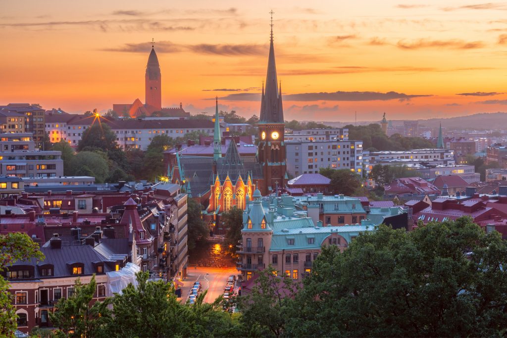 Ein warmes Abendrot liegt über Dächern und einer hell erleuchteten Kirche in der Stadt.