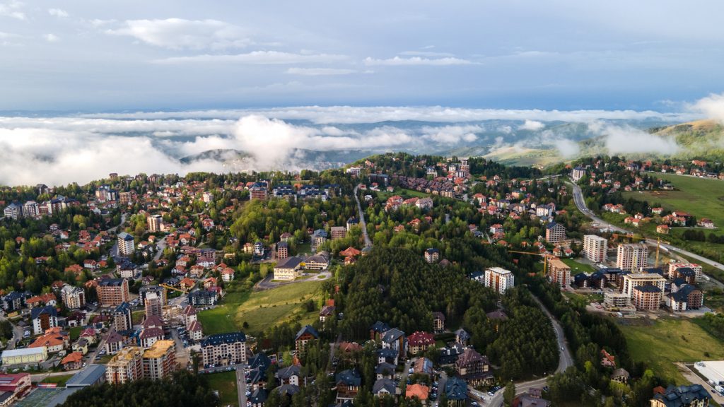 Luftaufnahme einer weitläufigen Bergsiedlung mit vielen Häusern, Wäldern und Wolken, die tief über den Hängen hängen.
