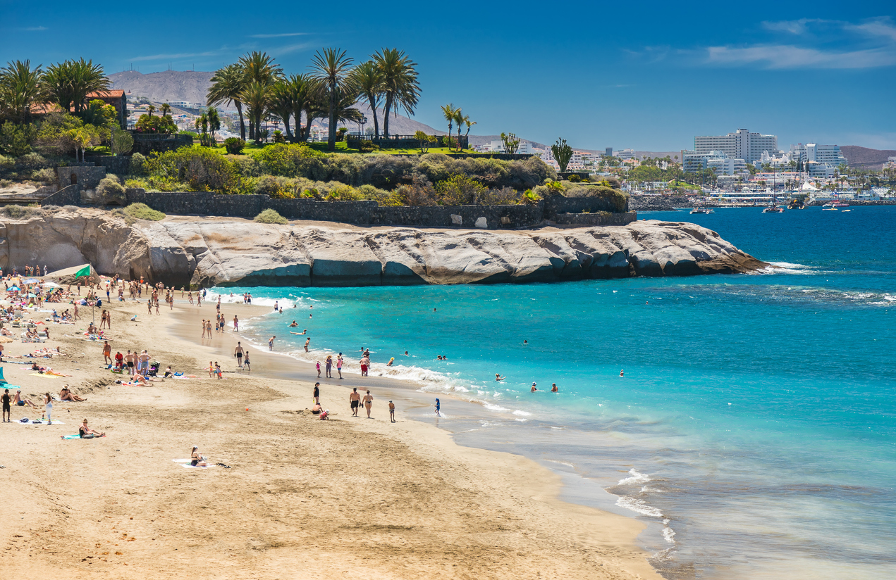 Breiter Strand der Playa del Duque mit türkisblauem Wasser, Badegästen und Hotels im Hintergrund.