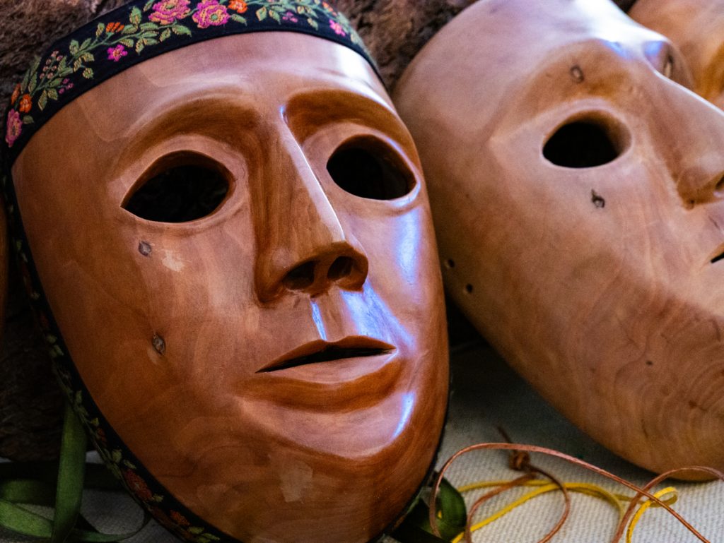 Zwei handgeschnitzte Masken liegen nebeneinander und zeigen glatte, braune Gesichter mit dunklen Augenöffnungen.