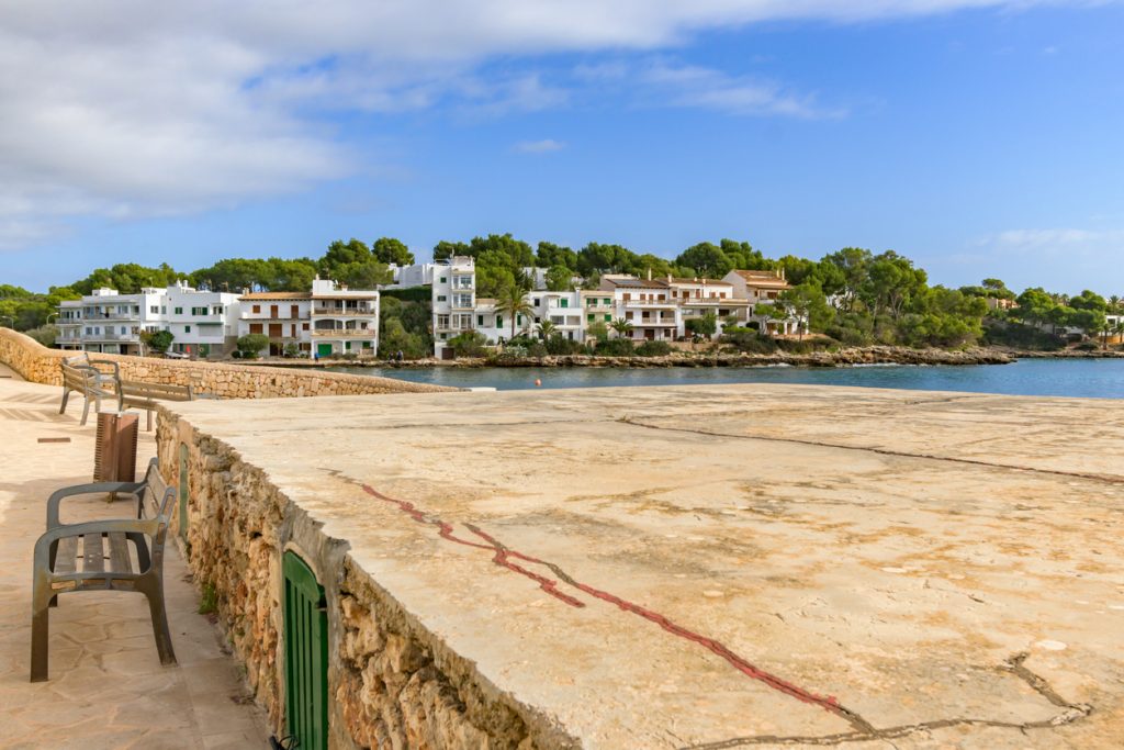 Eine breite Steinfläche und Sitzbänke führen am Meer entlang zu einer Häuserreihe am gegenüberliegenden Ufer.