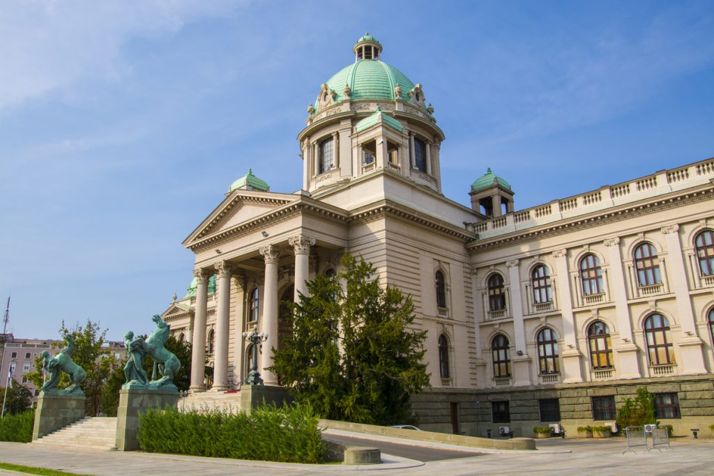 Klassizistisches Gebäude mit grüner Kuppel und Säulenfront bei blauem Himmel.