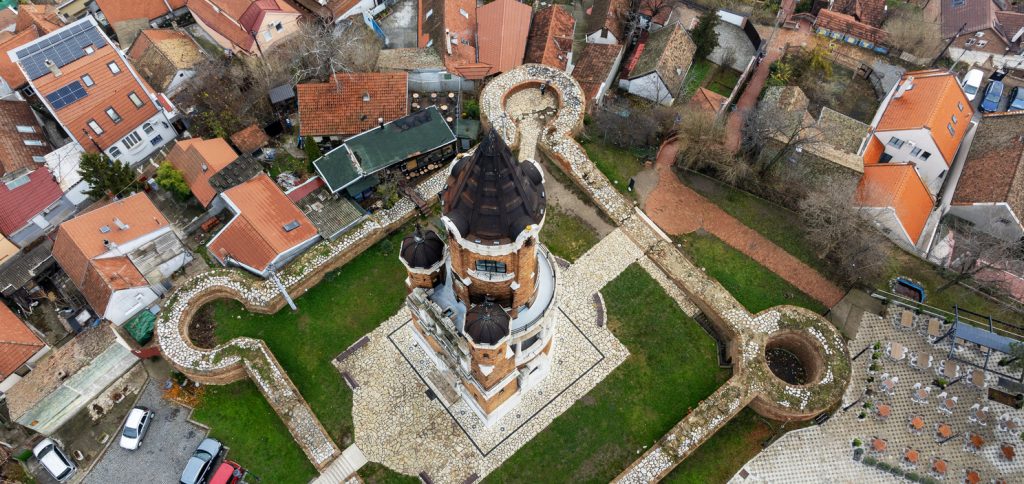 Luftaufnahme eines Turms mit kleiner Festungsmauer in einem Viertel mit Ziegeldächern.