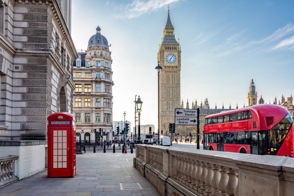 Eine rote Telefonzelle und ein roter Bus stehen nahe dem Elizabeth Tower.