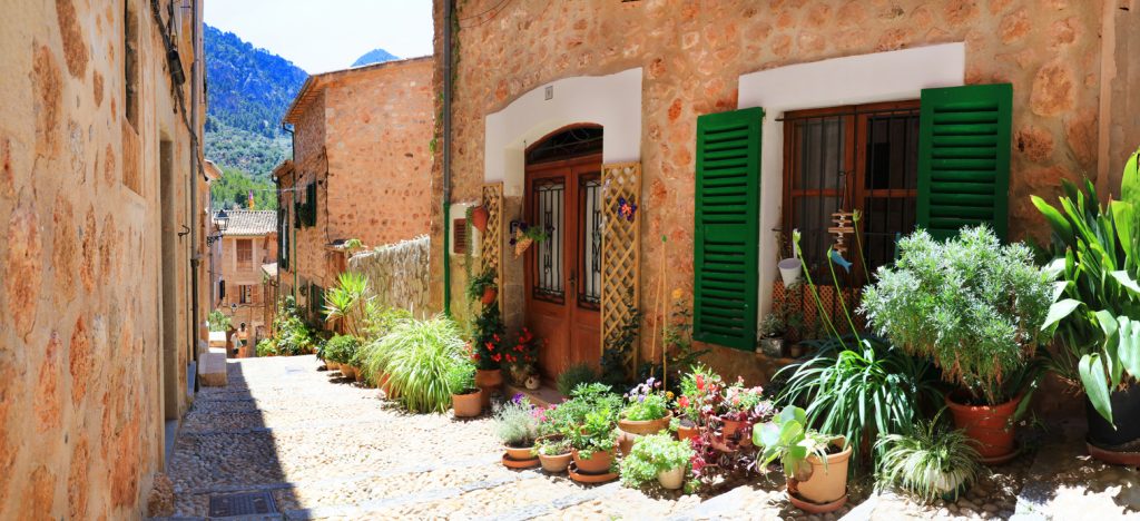 Enge Gasse mit Natursteinhäusern, grünen Fensterläden und vielen Pflanzen in Fornalutx.