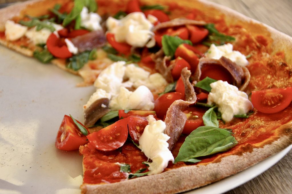 Eine dünne Pizza ist mit Kirschtomaten, Basilikum, cremigem Käse und Sardellen belegt.