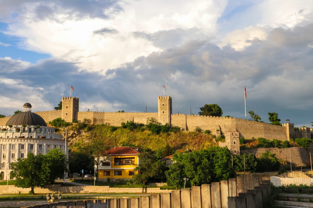 Eine lange Festungsmauer mit Türmen verläuft über einem Hügel am Rand der Stadt Skopje.