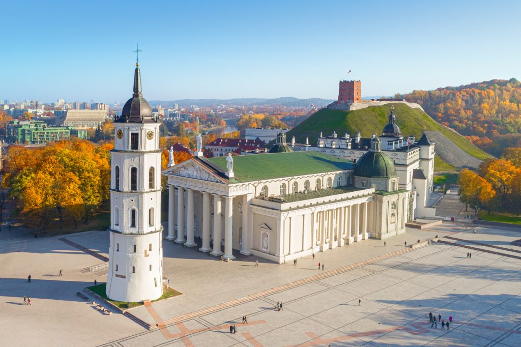 Der weiße Dom von Vilnius steht vor dem Gediminas-Turm, umgeben von herbstlichen Bäumen.