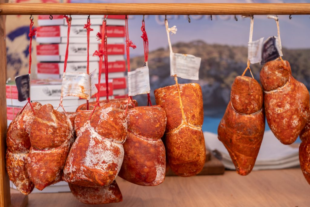 Mehrere rotbraune Sobrasada-Würste hängen an einer Stange an einem Marktstand.