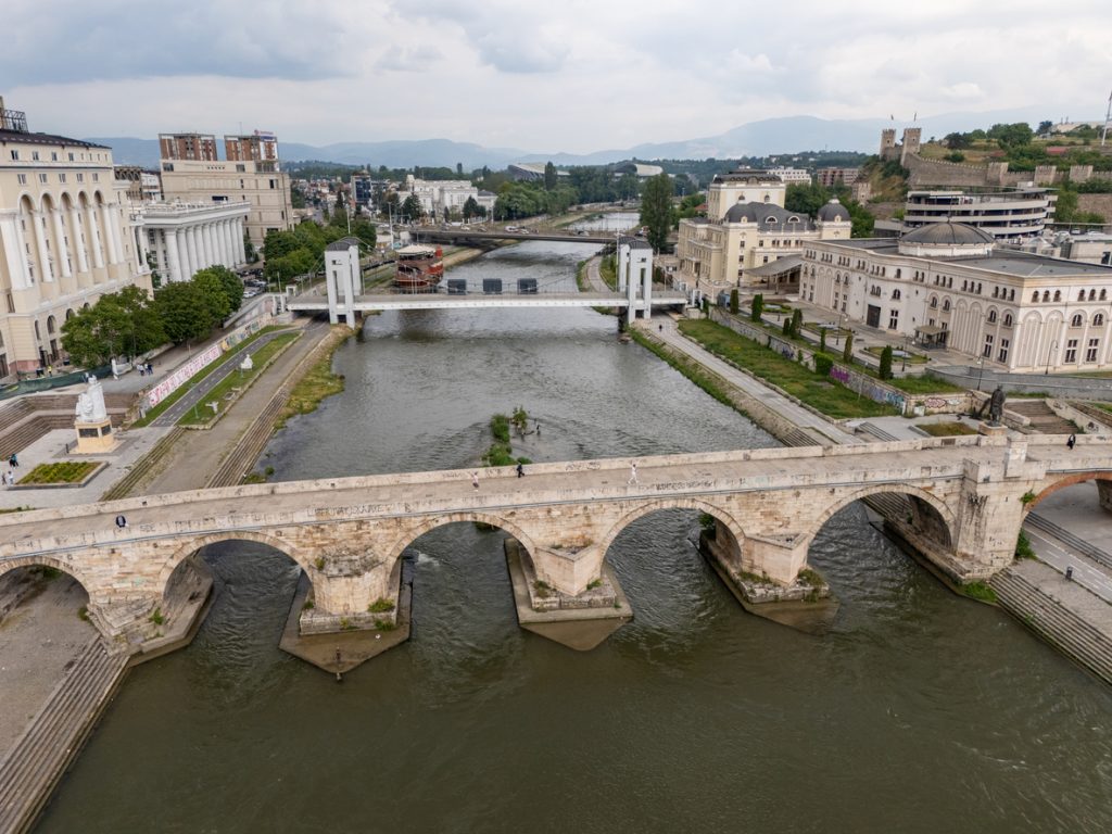 Blick auf eine alte Steinbrücke über den Fluss mit Stadtgebäuden im Hintergrund in Skopje.
