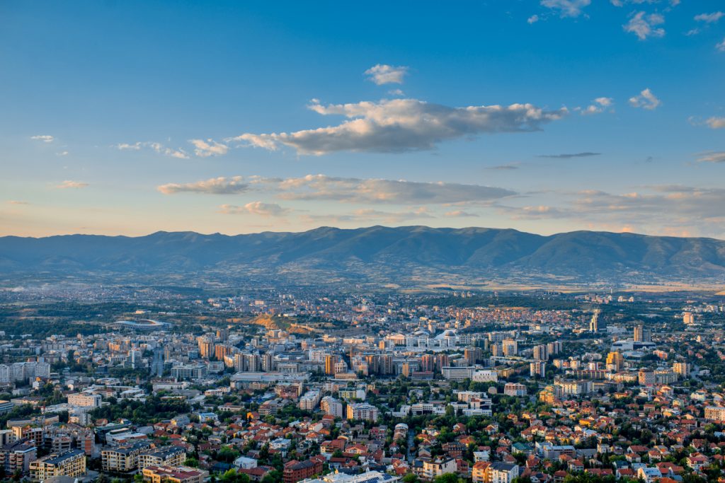 Weitblick über die Stadt mit vielen Dächern, Hochhäusern und Bergen am Horizont in Skopje.
