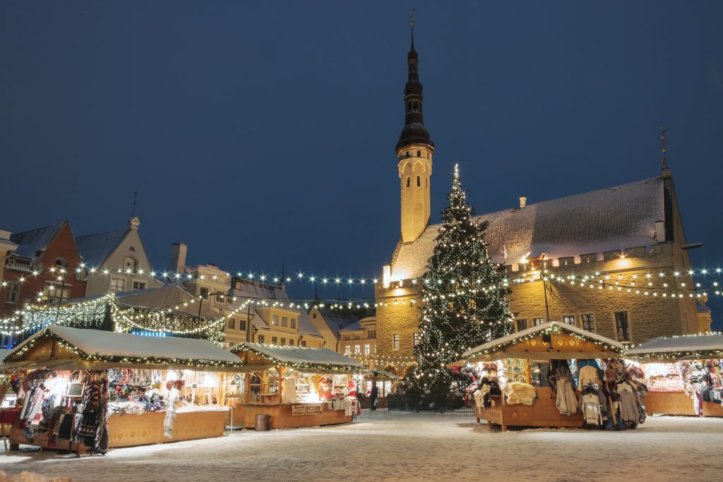 Weihnachtsmarkt bei Nacht mit beleuchtetem Baum, Buden und Turm im Hintergrund.