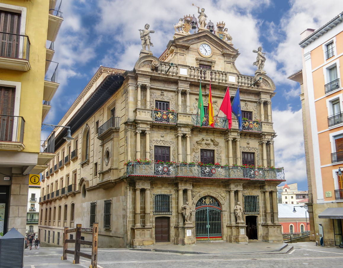 Historisches Rathaus mit Uhr und Flaggen auf einem Platz in Pamplona.