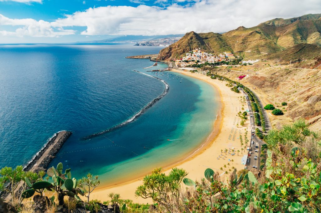 Blick von oben auf die Playa de Las Teresitas mit türkisblauem Wasser, langem Sandstrand und Bergen im Hintergrund.