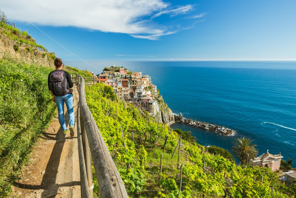 Wanderer auf Pfad mit Blick auf Küstendorf und tiefblaues Meer in den Cinque Terre.
