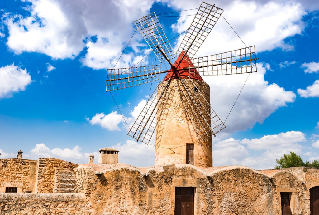 Historische Steinwindmühle mit roter Kappe und Gitterflügeln unter blauem Himmel auf Mallorca.