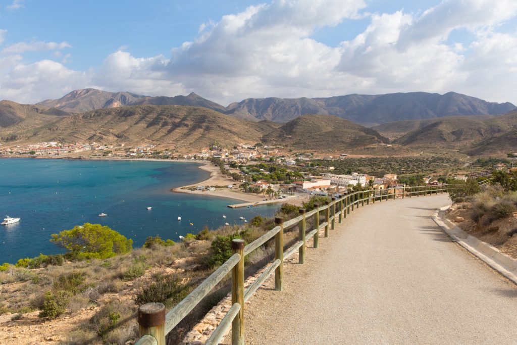 Ein asphaltierter Weg entlang der felsigen Küste führt zu einem kleinen Fischerdorf am Fuße der Berge