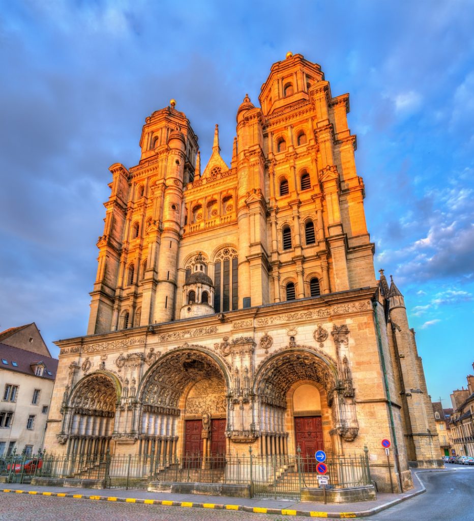 Die gotische Westfassade der Kathedrale von Dijon mit zwei markanten Türmen wird vom Abendlicht golden angestrahlt.