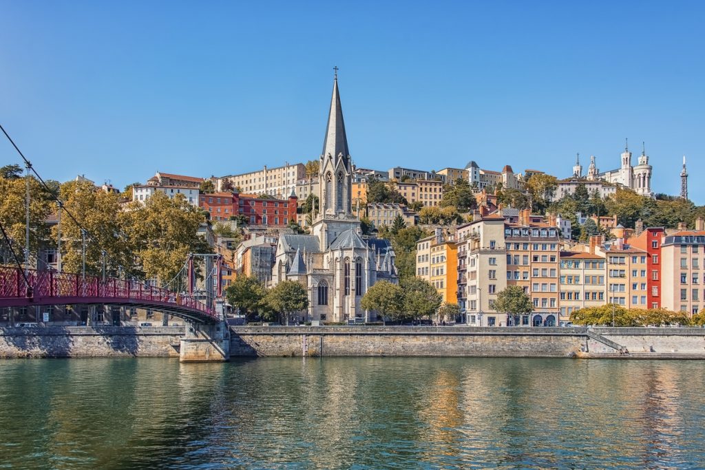 Uferansicht in Lyon mit Kirche, Brücke und bunten Gebäuden am Fluss.