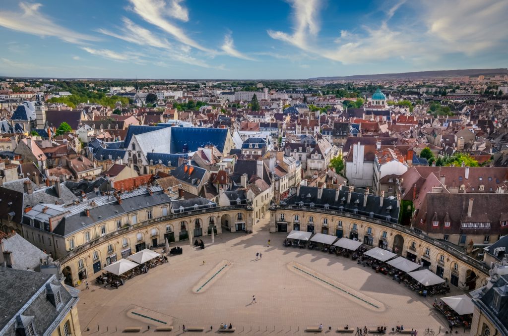 Eine Luftaufnahme des halbkreisförmigen Place de la Libération in Dijon, umgeben von historischen Gebäuden unter blauem Himmel.
