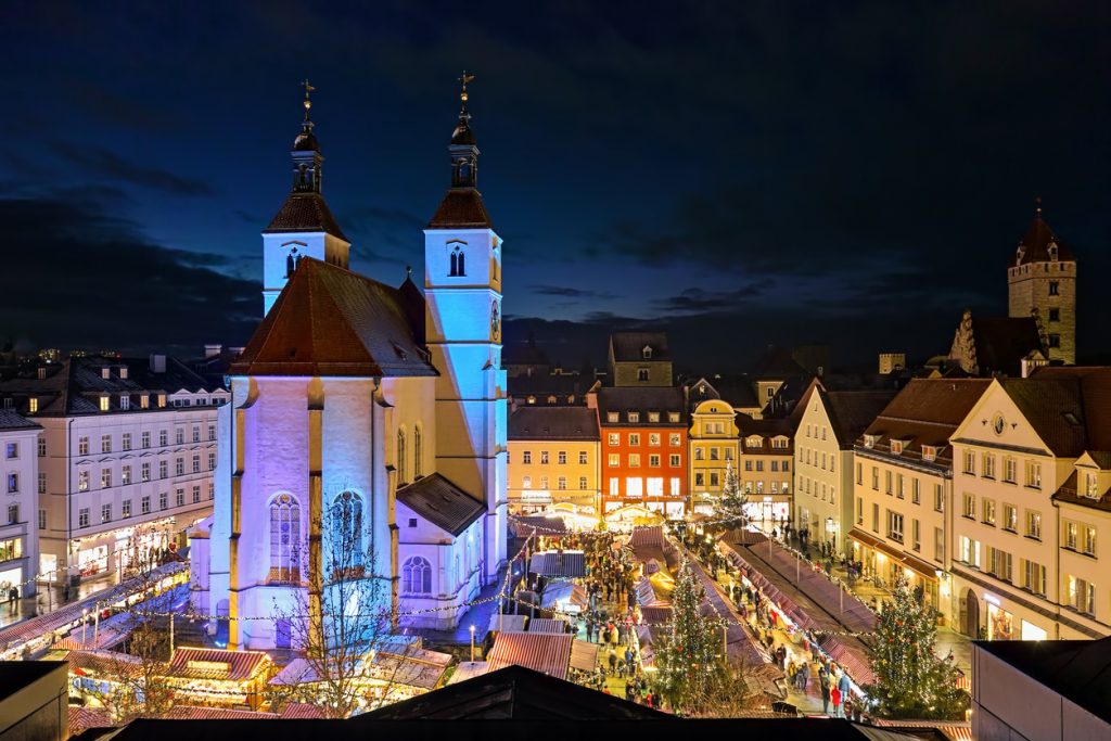 Der beleuchtete Neupfarrplatz in Regensburg bei Nacht mit festlich geschmückten Buden rund um die blau angestrahlte Neupfarrkirche.