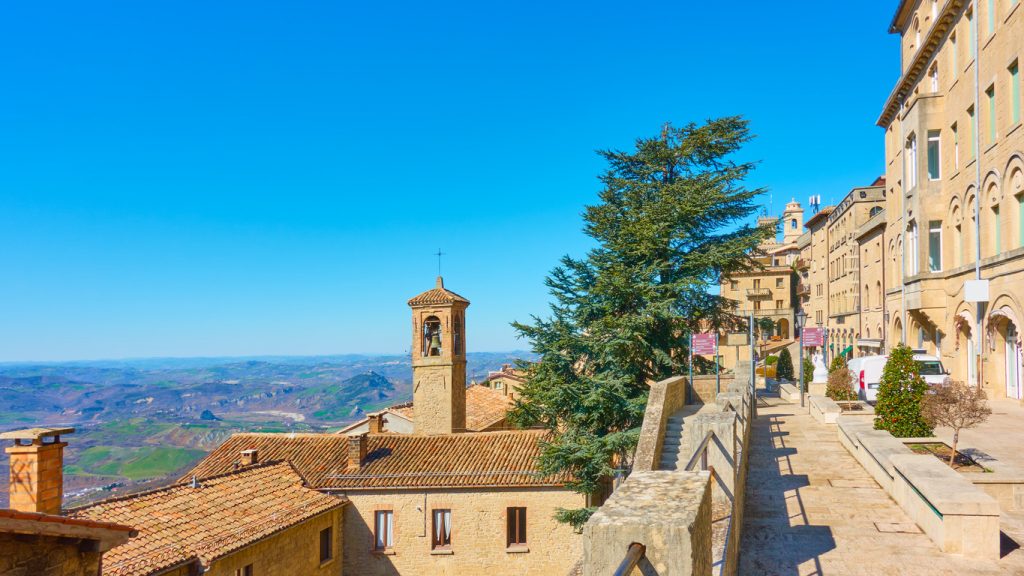 Ein gepflasterter Weg in San Marino mit Blick auf einen alten Glockenturm und die umliegende Bergwelt