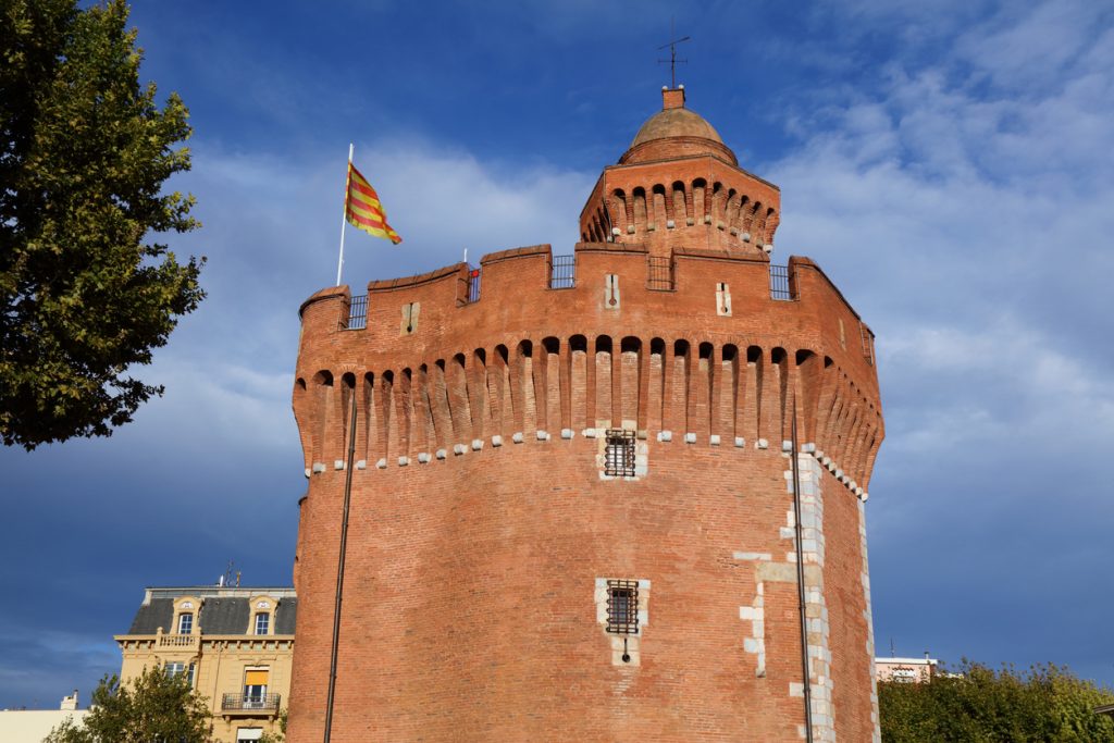 Massiver Backsteinturm mit Flagge vor blauem Himmel in Perpignan.