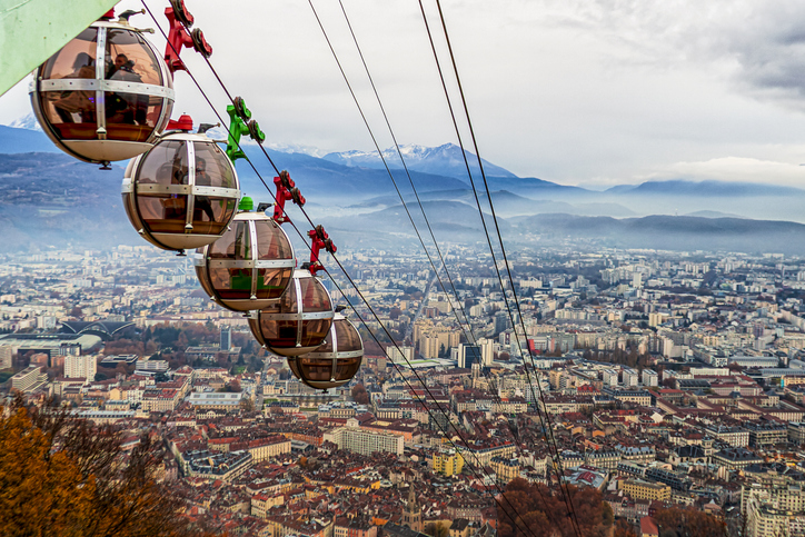 Die runden Glaskabinen der Bastille-Seilbahn schweben hoch über dem dichten Häusermeer von Grenoble vor einer nebligen Bergkulisse.
