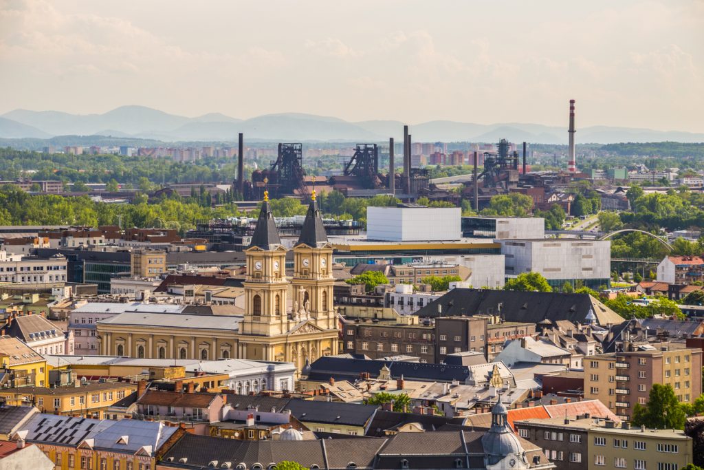 Blick über Dächer mit großer Kirche im Vordergrund und Industrieanlagen in der Ferne.
