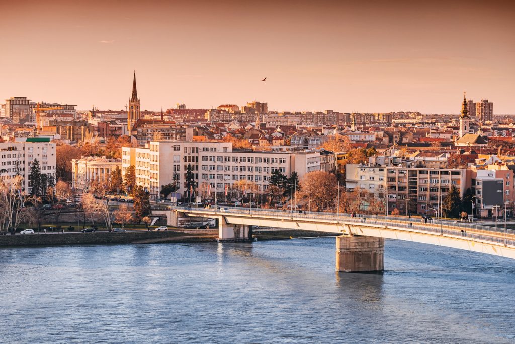 Eine Brücke führt über die Donau in die Stadt Novi Sad, die im warmen Licht des Sonnenuntergangs liegt.