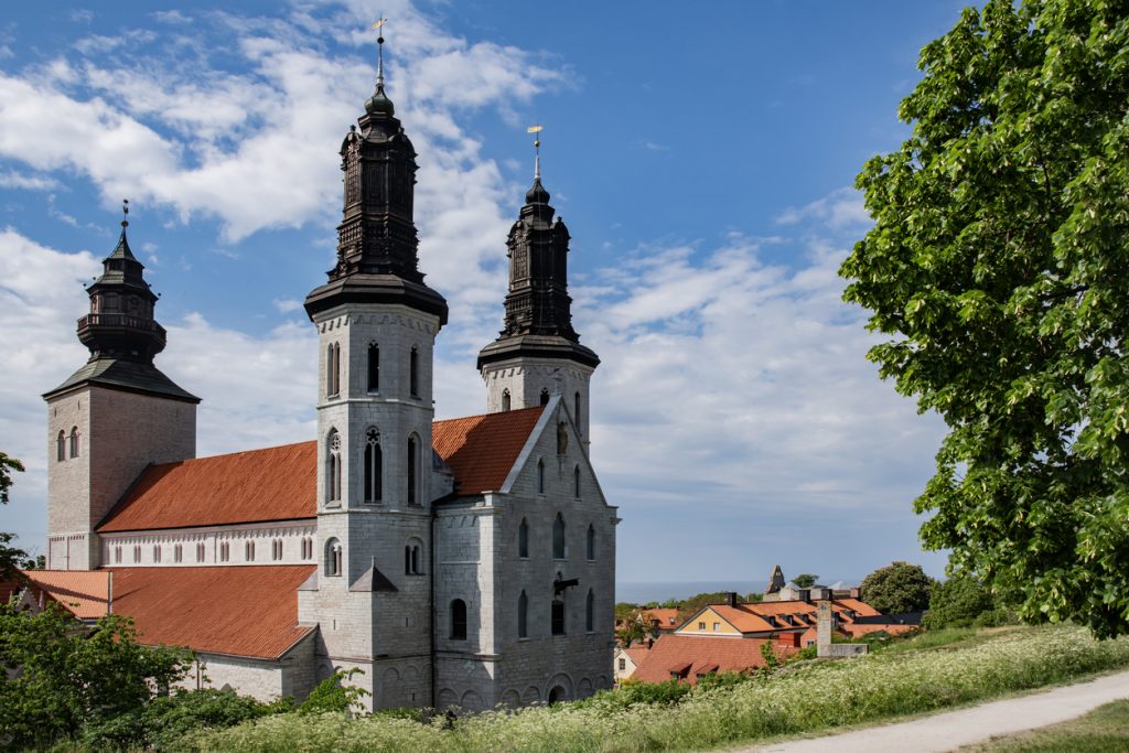 Große Kirche mit drei Türmen über roten Dächern bei blauem Himmel.