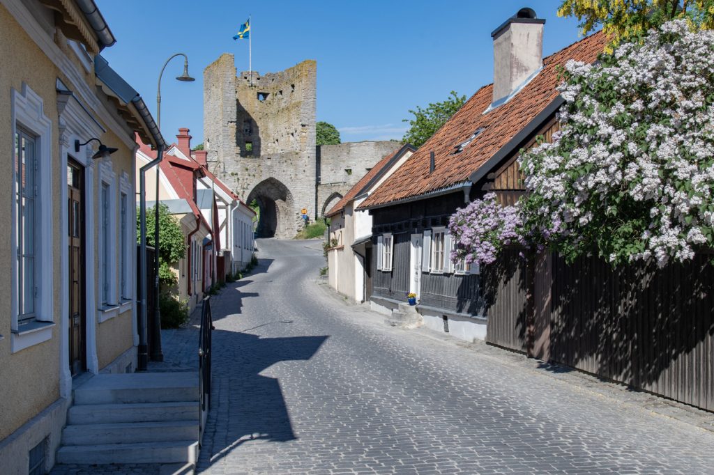 Kopfsteinpflasterstraße mit bunten Häusern und Stadttor im Hintergrund.