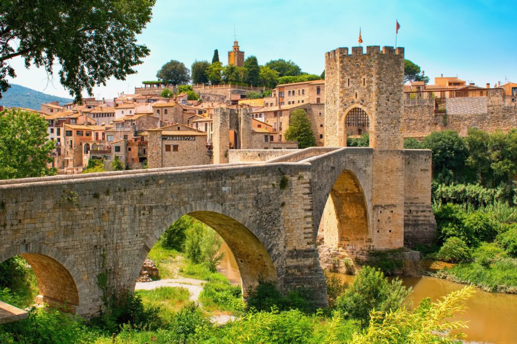 Eine massive mittelalterliche Steinbrücke mit einem befestigten Torturm führt über einen Fluss in die Altstadt nahe Girona.
