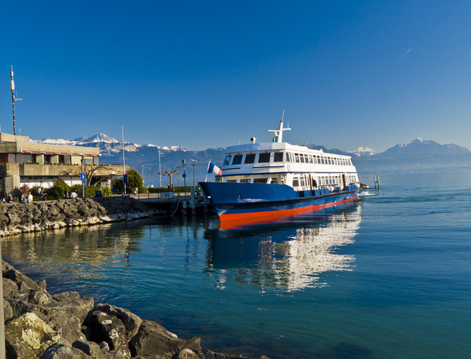 Passagierschiff legt am Ufer von Lausanne am Genfersee vor Bergkulisse an.