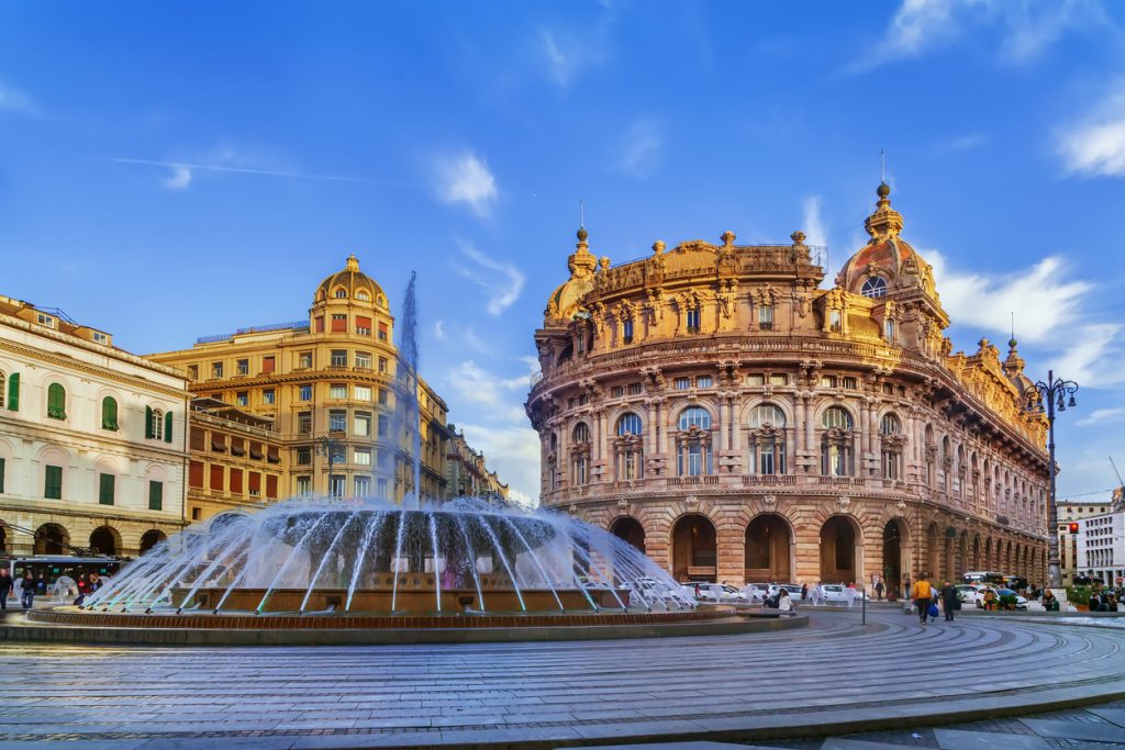 Der große kreisförmige Springbrunnen in Genua vor der prachtvollen Fassade des Palazzo della Nuova Borsa bei Abendlicht.