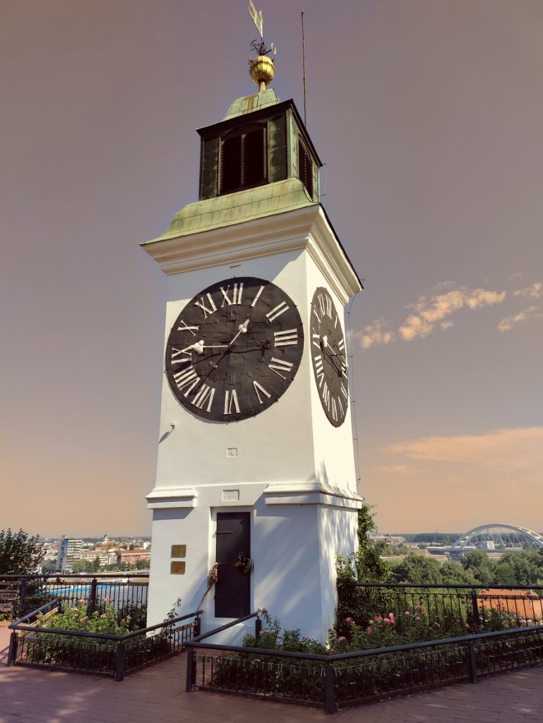Der weiße Uhrturm der Festung Petrovaradin steht vor einem leicht rötlichen Himmel.