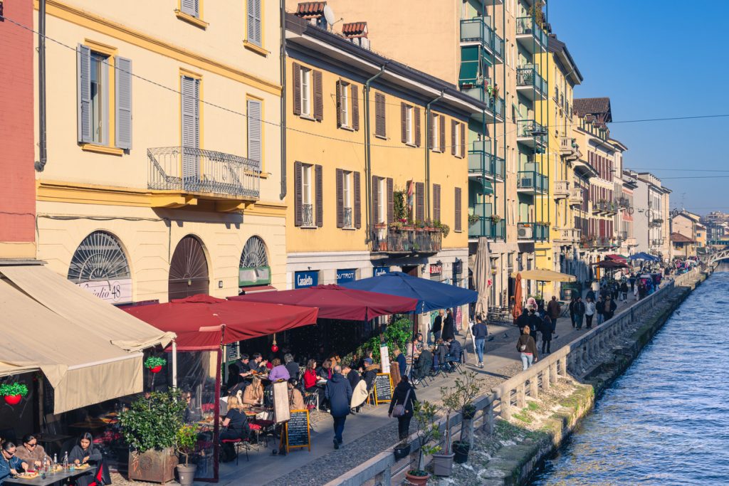 Café-Terrassen und Spaziergänger an einem Kanal in Mailand bei Tageslicht.