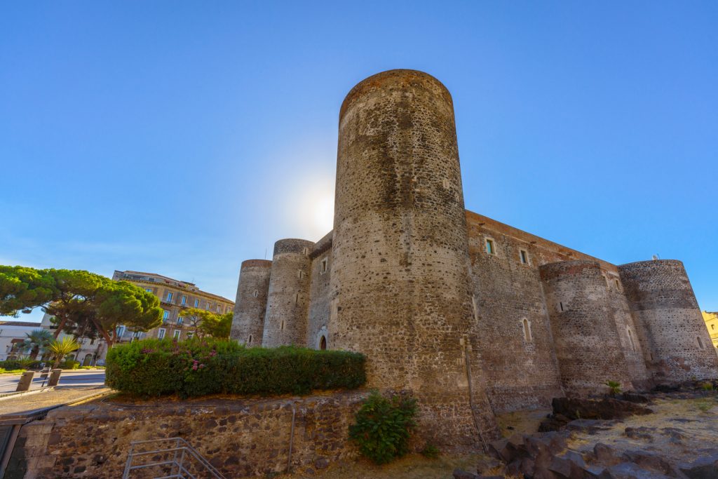 Die massiven Rundtürme des Castello Ursino ragen vor blauem Himmel auf.